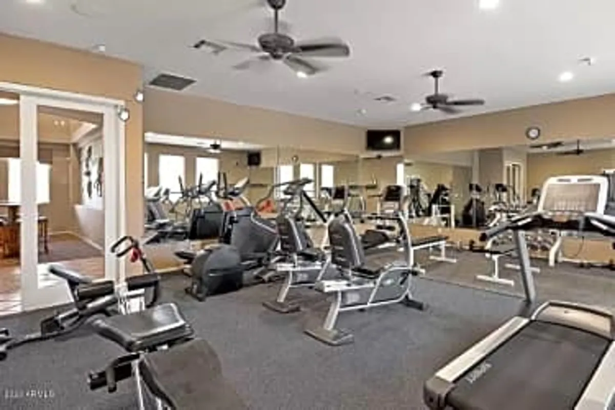 A bright and spacious fitness facility featuring treadmills, exercise bikes, and weight machines along a mirrored wall. The room is filled with natural light, offering a motivating and energetic environment for workouts or quick exercise breaks.