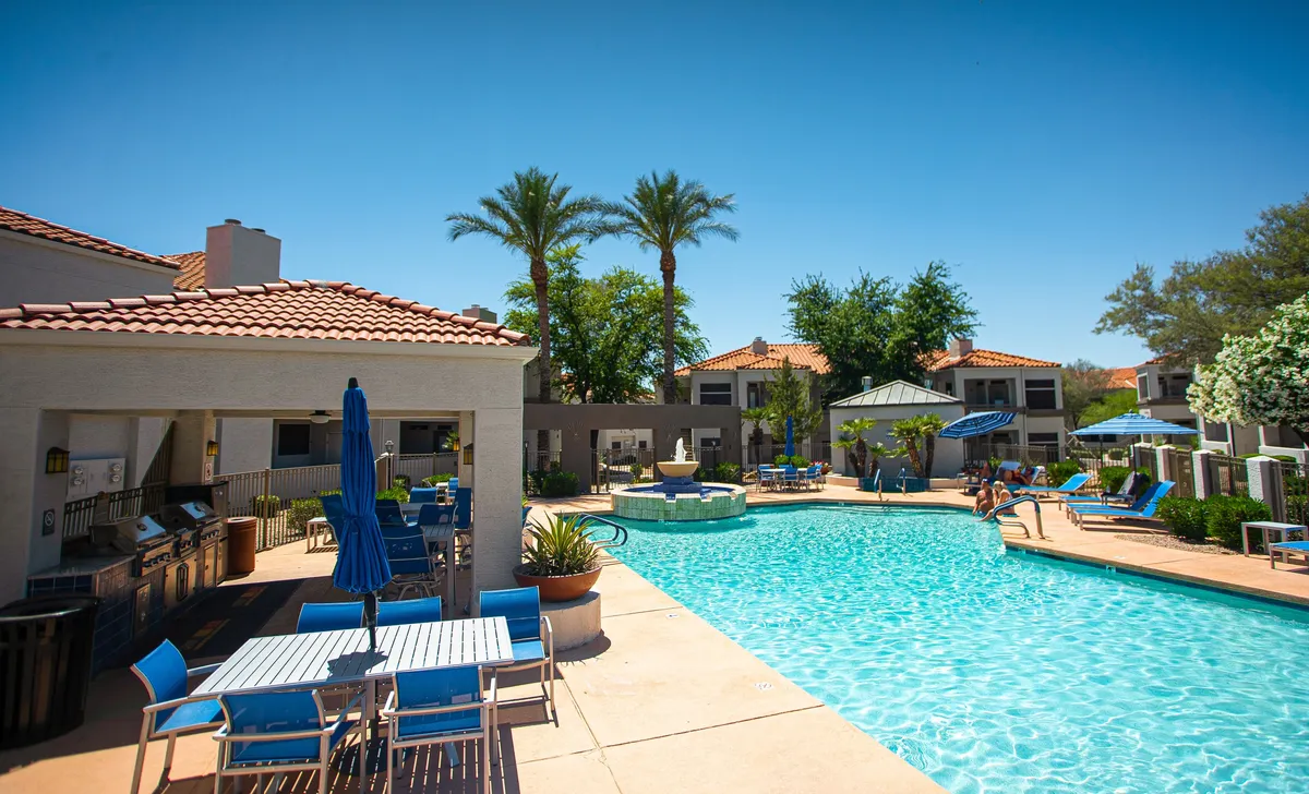 A vibrant exterior shot showcasing a sparkling swimming pool surrounded by palm trees, comfortable lounge chairs, and an inviting outdoor seating area. A barbecue grill is visible in the background, emphasizing opportunities for relaxation and social gatherings.