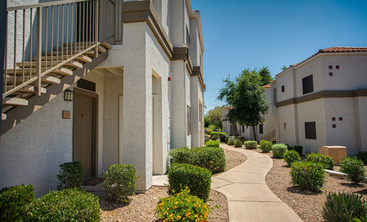 A welcoming exterior view shows landscaped shrubs, flower beds, a prominent front staircase, and pathway leading to the entrance. The vibrant foliage and accessible entryway evoke a sense of safety, comfort, and neighborly charm—important for medical travelers prioritizing ease of movement.