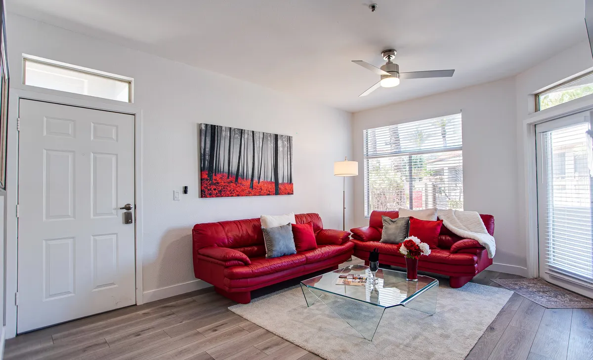 A warm and inviting living area featuring red sofas, a glass coffee table, and colorful artwork on the wall. The setup encourages relaxation, socializing, and unwinding after a busy day.