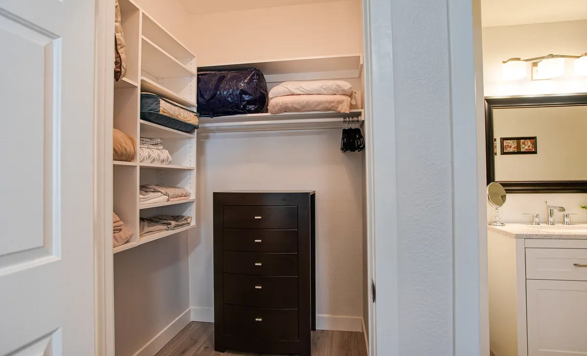 Shelves lined with neatly arranged linens and a dark wooden dresser demonstrate ample storage space. The calm, tidy mood highlights how guests can easily organize their belongings and access fresh towels and seasonal blankets.