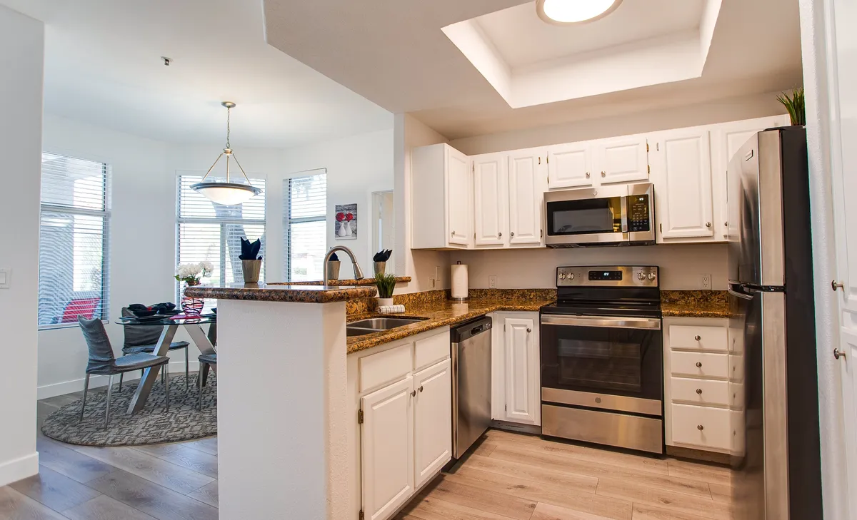 An open-concept space that seamlessly combines the kitchen and dining area, featuring a granite countertop, stainless steel appliances, dining table, and large windows that bathe the space in natural light.