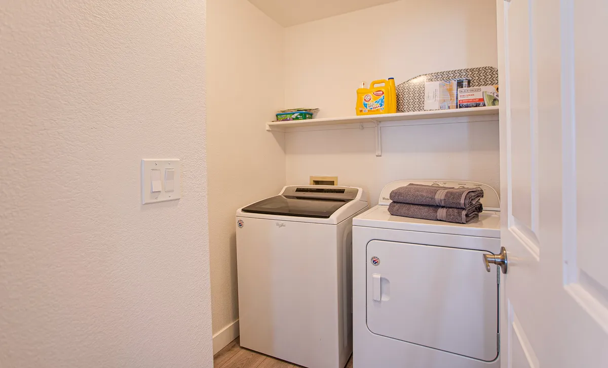 This image showcases a washer and dryer tucked neatly into a dedicated laundry area, with a shelf holding laundry supplies and folded towels. The setup is practical, clean, and organized, emphasizing convenience and functionality.