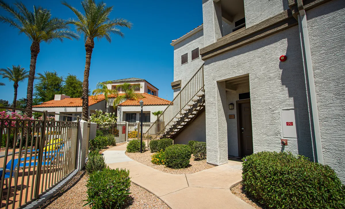 This image captures the inviting exterior of the property, featuring tall palm trees, lush landscaping, and a view of the building architecture. The tranquil, sunlit environment hints at resort-style amenities and a peaceful community atmosphere, ideally suited for guests seeking relaxation and accessibility.