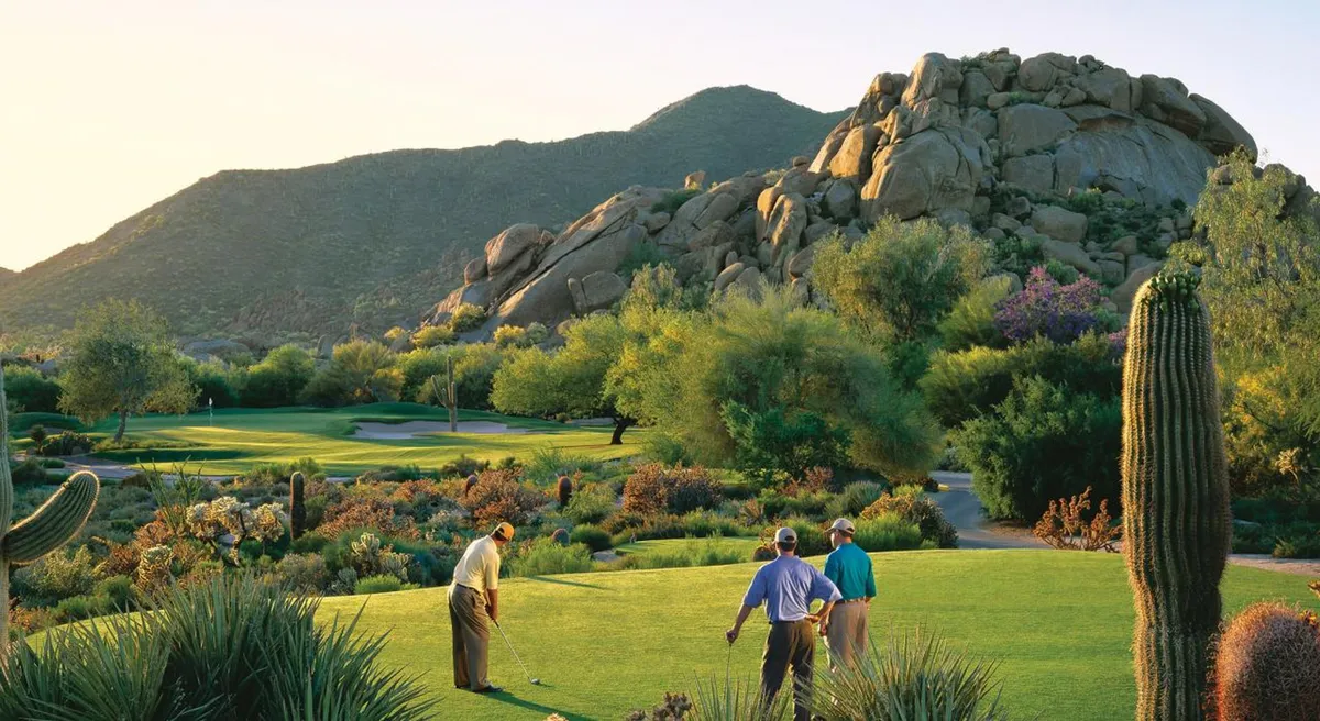 A vibrant exterior scene of golfers preparing to take shots on a lush course, surrounded by iconic cacti, desert vegetation, and a mountainous backdrop. The atmosphere is active yet relaxed, with participants socializing and enjoying the outdoors.