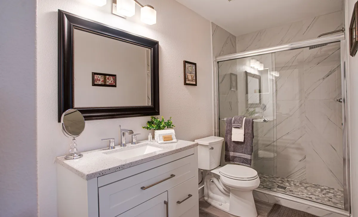 A bright, modern bathroom with a vanity and sink, large mirror, glass shower enclosure, and tasteful wall art. The refreshing ambiance invites peaceful moments for morning routines or evening wind-downs.