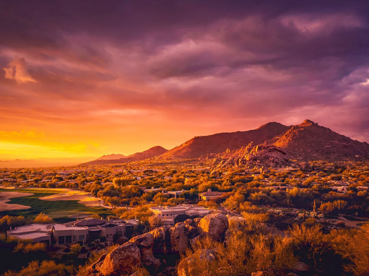 A scenic landscape of Scottsdale with dramatic mountains, a lush golf course, and distinctive desert rock formations. The broad view highlights the region's unique natural beauty and opportunities for outdoor recreation.